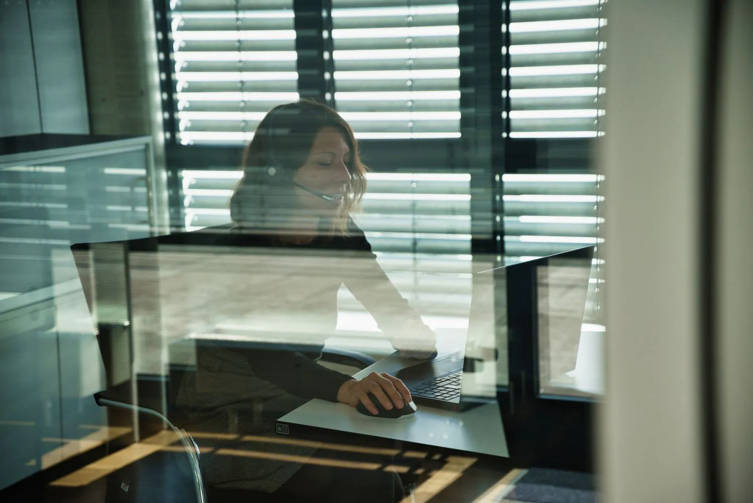 Blick durch Glaswand auf arbeitende Frau am Schreibtisch