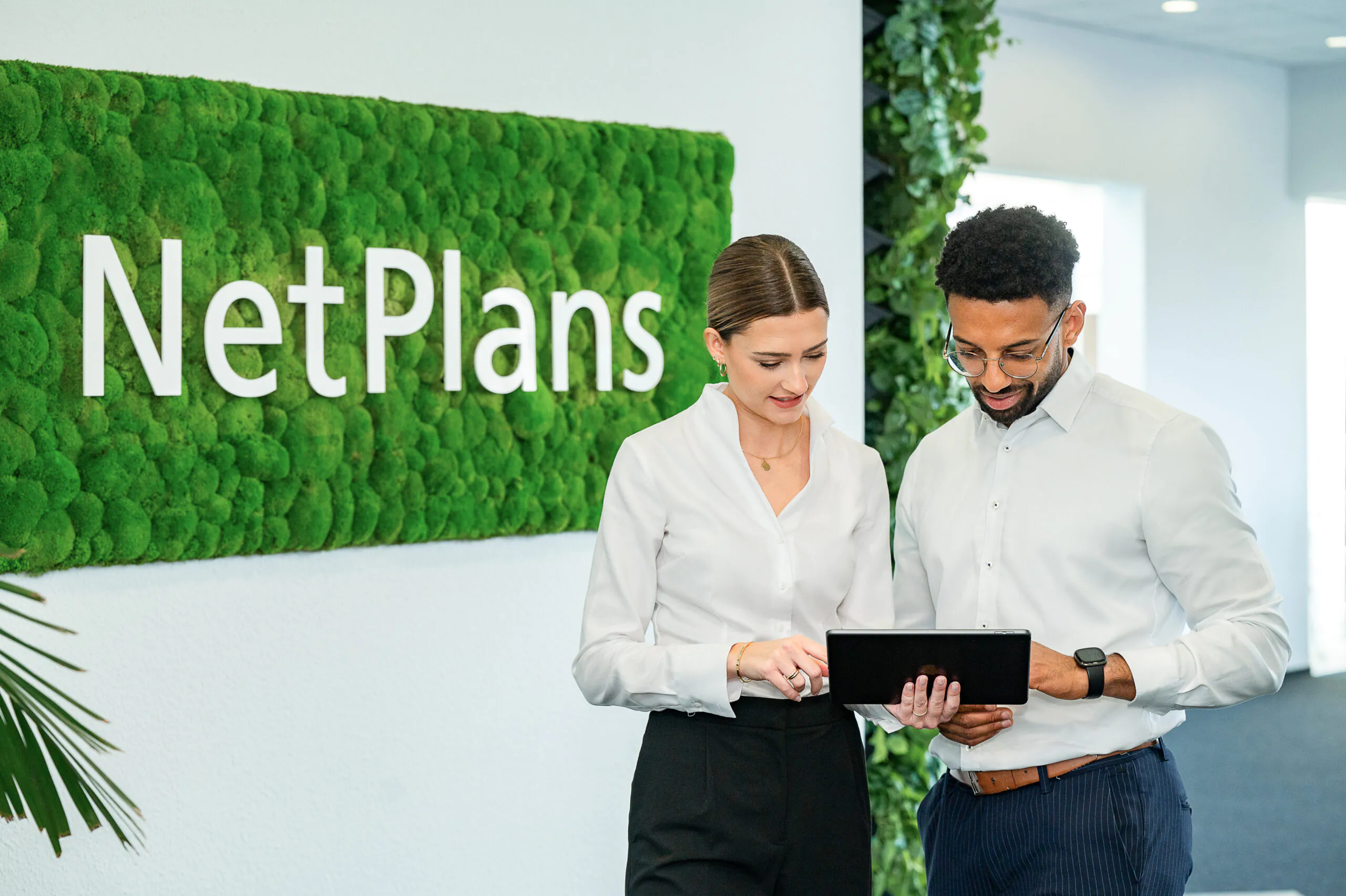 Absprache zweier Geschäftskollegen auf Tablet vor Netplans Schriftzug im Bürogang