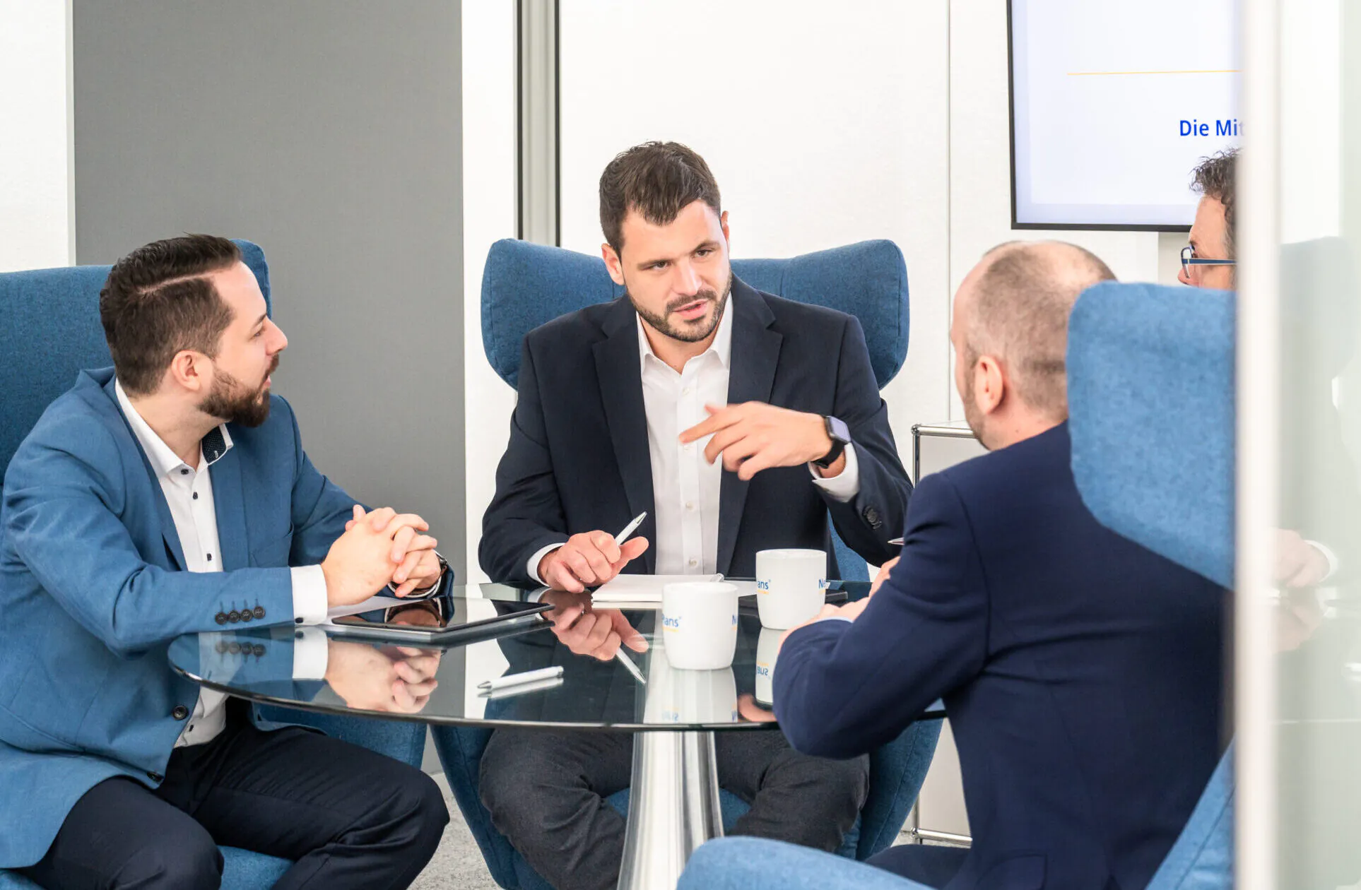 Geschäftsgespräch an rundem Glastisch von vier Männern auf Stühlen mit hoher Lehne